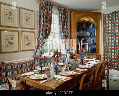 Rosso, bianco e blu controllato tende e cuscini e nella sala da pranzo con le regolazioni del posto su rettangolare tavolo in legno Foto Stock