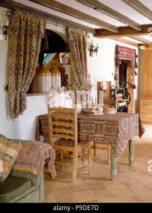 Tende a motivi geometrici sulla finestra sopra la tabella con abbinamento di panno e sedie ladderback cottage in sala da pranzo Foto Stock