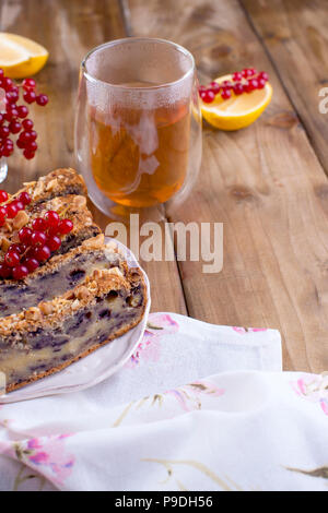 In casa torta dolce per la prima colazione con il limone e le bacche di ribes nero e ribes rosso. Un bicchiere di tè. In legno marrone e sfondo spazio libero per il testo o una cartolina Foto Stock