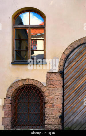 Finestra con un riflesso del cielo e il tetto con le vecchie porte e sbarre sulla facciata di una casa nella città vecchia di Riga Foto Stock
