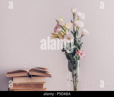 Eustoma bouquet di fiori in un vaso, una pila di vecchi libri vintage e ghirlanda di luci su uno sfondo grigio. Lettura e relax concept Foto Stock