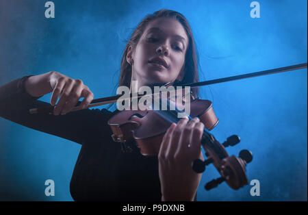 Bella giovane donna a suonare il violino contro uno sfondo scuro Foto Stock