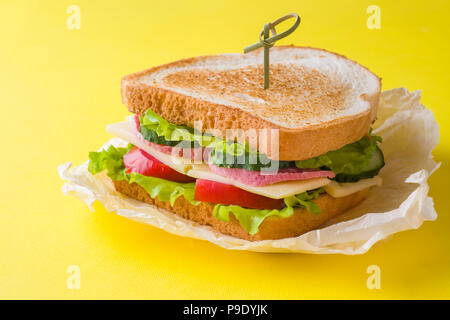 Sandwich con formaggio, prosciutto e verdure fresche in un giallo sfondo luminoso Foto Stock