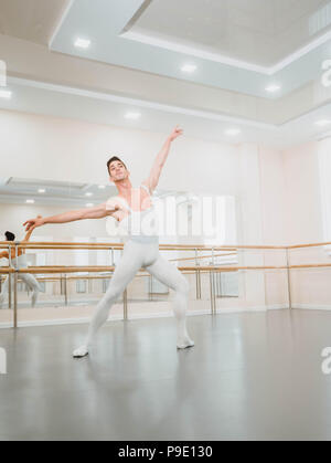 Bel giovane ballerino maschio pratica del balletto classico nel piccolo studio con specchi. Uomo in bianco collant. Professional coreografo sta lavorando sulla creazione di prestazioni. Foto Stock