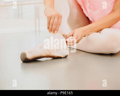 Giovane ballerina in tutù rosa avvolge il costume di nastri di seta bianca di soft top scarpe da ballo pointe e li collega. La donna la preparazione per la danza lezioni di training in palestra. Foto Stock