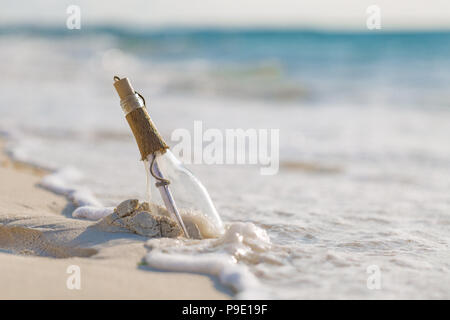 Messaggio in bottiglia sulla spiaggia con sabbia bianca, nel mare tropicale. Castaway e perdita di sfondo concettuale Foto Stock