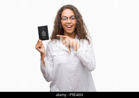 Giovane donna ispanica holding passaporto del Canada molto felice puntando con mani e dita Foto Stock