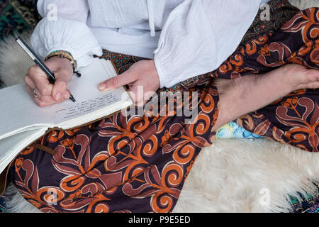 Elevato angolo di visione della donna che indossa pantaloni con motivo floreale seduta sul tappeto shag scrivendo nel diario. Foto Stock