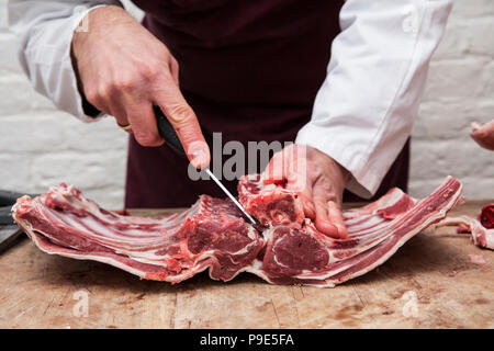 Un macellaio con un coltello affilato per preparare costolette di agnello per il carré di agnello. Foto Stock