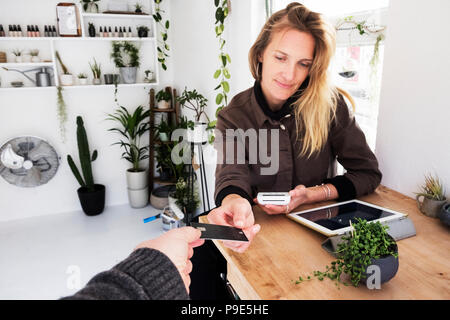 Proprietaria del negozio di impianto di ricezione carta di credito dal cliente per il pagamento di piccole perle impianto in pot nero. Foto Stock