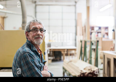 Ritratto di un senior Caucasian falegname in un grande negozio di macchine per la lavorazione del legno. Foto Stock