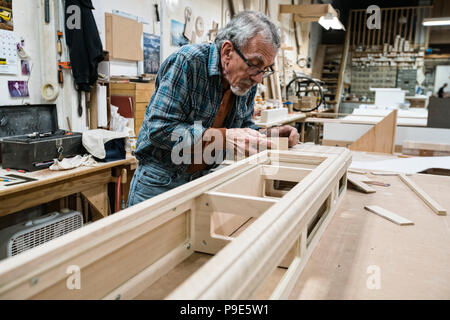 Senior carepenter caucasica la levigazione di un armadio in legno in parte in un grande negozio di macchine per la lavorazione del legno. Foto Stock