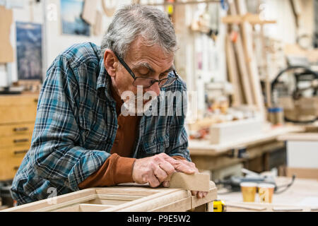 Senior carepenter caucasica la levigazione di un armadio in legno in parte in un grande negozio di macchine per la lavorazione del legno. Foto Stock