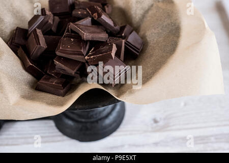 Pezzetti di cioccolato sulla carta oleata su una bilancia di pesatura. Foto Stock