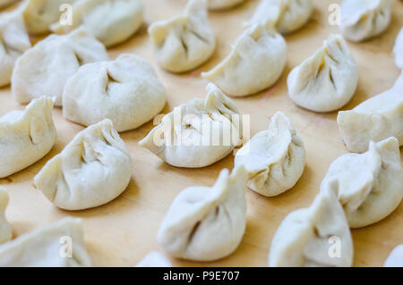 Close-up di cinese gnocco crudo posto sulla tavola di legno. Gnocco è chiamato Jiaozi in cinese, è un popolare cinese tradizionale cibo. Foto Stock