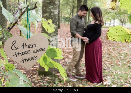 Giovane al di fuori nella soleggiata woodland holding baby bump, coccole Foto Stock