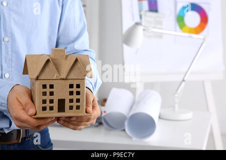 Imprenditore con casa miniatura in mano in piedi in ufficio Foto Stock