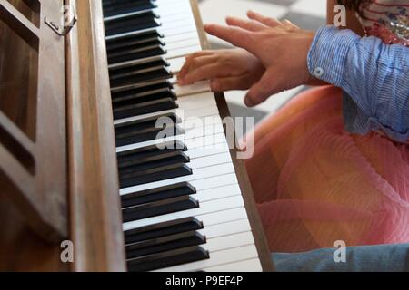 Lezione di piano: un adulto cerca di incoraggiare un bambino sul pianoforte di esempio Foto Stock