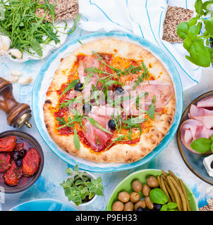 Il cibo italiano sul tavolo, pizza e antipasto. Bella che serve per una cena in famiglia. Olive e basilico. Formaggio e prosciutto. Foto Stock