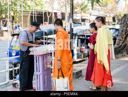 I monaci buddisti guarda una vecchia strada tailandese performer la riproduzione di musica sui bicchieri di acqua in Chiang Mai Thailandia Foto Stock