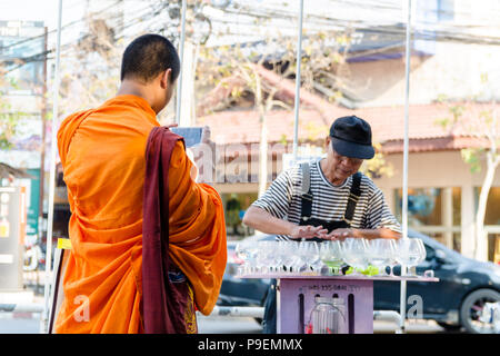 Monaco buddista di scattare le foto come una vecchia strada tailandese attore è la riproduzione di musica sui bicchieri di acqua in Chiang Mai Thailandia Foto Stock