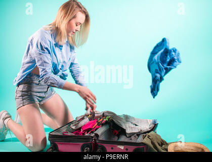 Vestiti di imballaggio., giovane donna bionda la scelta di cose necessarie per il viaggio .pack i bagagli. vista laterale foto Foto Stock