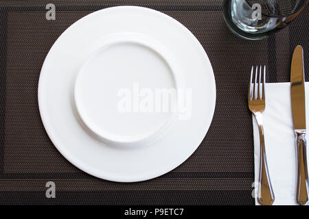 Bianco per le placche vuote con coltello e forchetta legate con un nastro su una tovaglia marrone Foto Stock