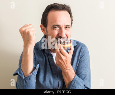 Senior uomo mangiare il cioccolato ciambella urlando orgoglioso e celebrando la vittoria e il successo molto eccitato, allietarla emozione Foto Stock