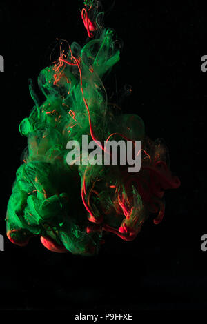 Il verde e il rosso dell'inchiostro che fluisce in acqua e miscelare insieme su uno sfondo nero. Foto Stock