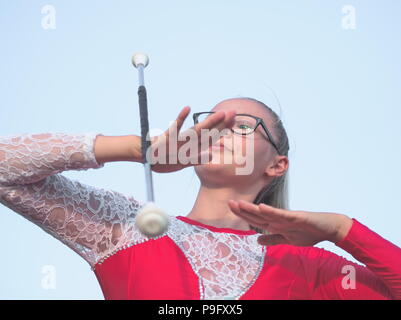 Bespectacled Blonde Teen Majorette ragazza fa roteare Baton all aperto in abito rosso Foto Stock