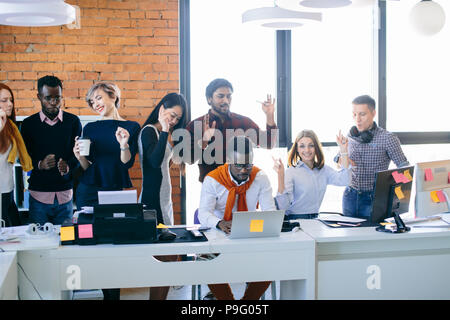 Giovani aziende diverse persone stanno avendo parte al lavoro mentre il loro collega africano sta lavorando sul computer portatile in ufficio con soppalco interno Foto Stock