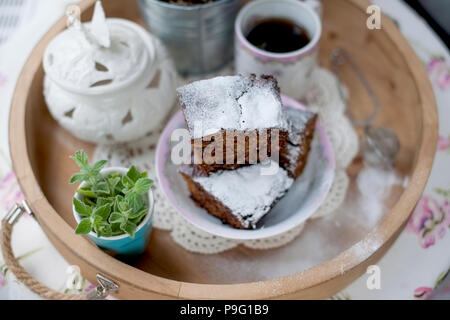 Tortina di cioccolato con zucchero e caffè. La colazione su un vassoio di legno e fiori. Foto Stock
