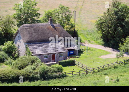 Stile tradizionale costruito in pietra Casale con tetto di paglia e piastrelle di ardesia, impostato in inglese bella campagna verde su una soleggiata giornata estiva Foto Stock