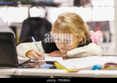 Poco carino ragazza studiare o fare i compiti tenendo pen, studio nella scuola Foto Stock