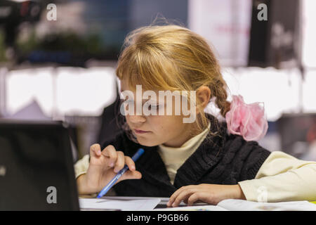 Poco carino ragazza studiare o fare i compiti tenendo pen, studio nella scuola Foto Stock