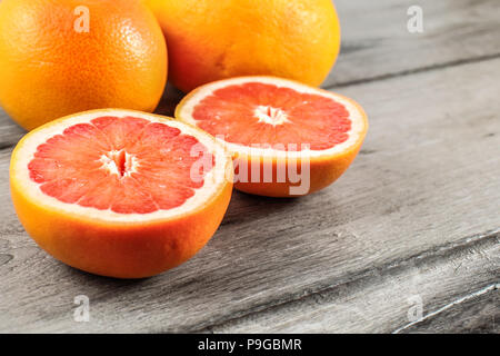 Rosa rosso pompelmo tagliato a metà con due interi in sfondo grigio sulla tavola di legno. Foto Stock