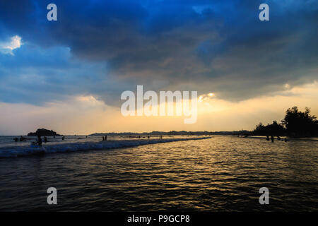 Tramonto sull'oceano in un giorno nuvoloso, sagome di surfers nell'oceano Foto Stock