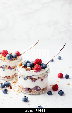 Due vasi con gustosi parfaits fatta di granola, bacche e yogurt greco bianco su un tavolo di legno. Girato l'angolo. Foto Stock