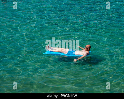 Un uomo che galleggia su un gommone in un mare limpido e cristallino Foto Stock