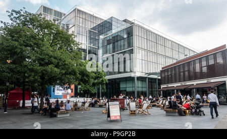 Persone relax sulle sdraio o panche di legno in chat con i Vescovi Square, una proprietà privata di spazio pubblico in Spitalfields London. Patisserie Valerie Foto Stock