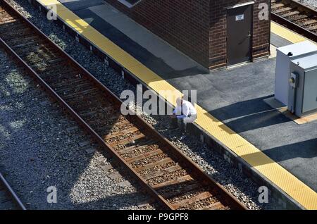 Rosemont, Illinois, Stati Uniti d'America. Un " commuter " lone siede sul giallo di avvertimento sezione della stazione ferroviaria in attesa di un treno in corrispondenza di una stazione di Metra. Foto Stock