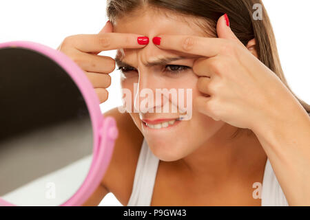 Giovane donna che guarda a se stessa nello specchio e la spremitura brufoli Foto Stock