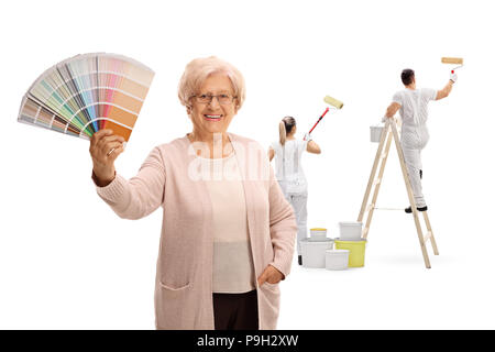 Donna matura tenendo un campione di colore con due pittori pittura dietro il suo isolato su sfondo bianco Foto Stock