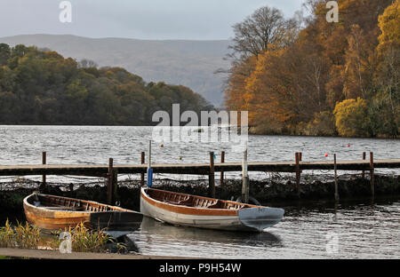 Le foglie di autunno sugli alberi salendo dalla sponda orientale del Loch Lomond in Scozia con ormeggiate le barche a remi e jetty in primo piano. Foto Stock