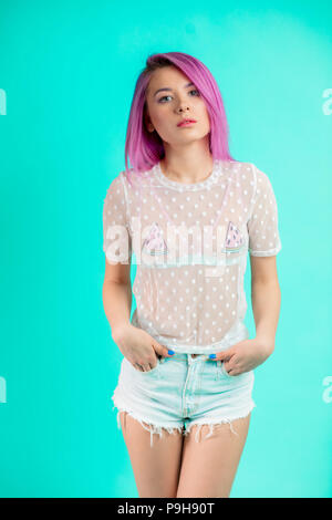 Bella femmina modello con violetto rosa acconciatura, vestito in estate camicetta romantico e gli shorts in denim in piedi isolato su sfondo blu Foto Stock