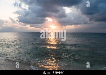 Bellissimo paesaggio tropicale - con enormi nuvole temporalesche proveniente da sopra la superficie dell'acqua e sole riflettendo in più scuro della superficie dell'acqua con una piccola isola nera Foto Stock