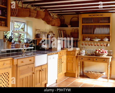 Collezione di ceste sul soffitto sopra il lavabo e lavastoviglie in cottage di legno cucina con piastra sopra a cremagliera lato tavolo Foto Stock