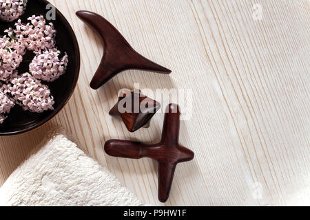 SPA e massaggi concetto. Massaggio in legno bastoni, asciugamani in spugna, Vaso con fiori su sfondo di legno. Foto Stock