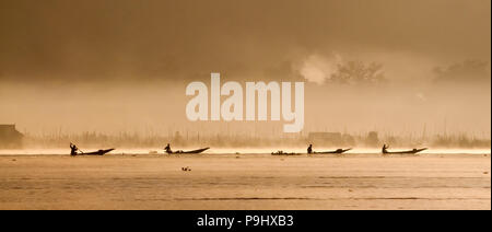 Sagome di quattro pescatori sulle barche in Myanmar (Birmania) andare al Lago Inle durante l alba con nebbia di mattina Foto Stock