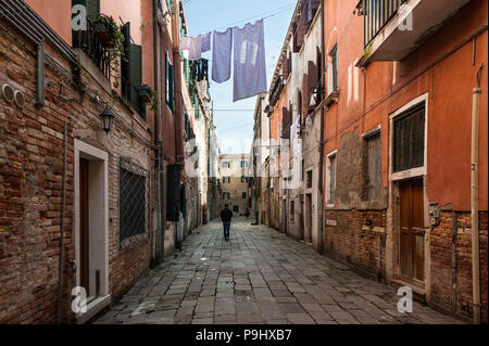 Un uomo che cammina su un quasi vuoto street sotto l'asciugatura biancheria da letto a Venezia, Italia Foto Stock